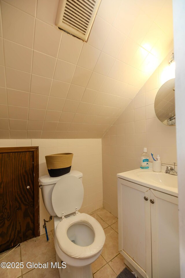 bathroom with vanity, lofted ceiling, tile walls, toilet, and tile patterned floors