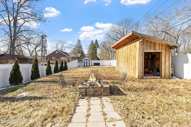 view of yard with an outbuilding, a storage unit, a fire pit, and a fenced backyard