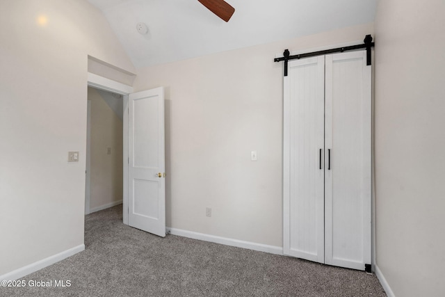 unfurnished bedroom featuring vaulted ceiling, a barn door, carpet, and baseboards