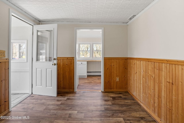 empty room featuring wood finished floors, a wainscoted wall, plenty of natural light, and a baseboard heating unit