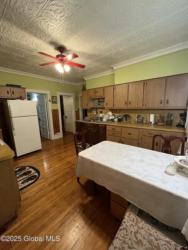 kitchen featuring ornamental molding, an ornate ceiling, freestanding refrigerator, wood-type flooring, and brown cabinetry