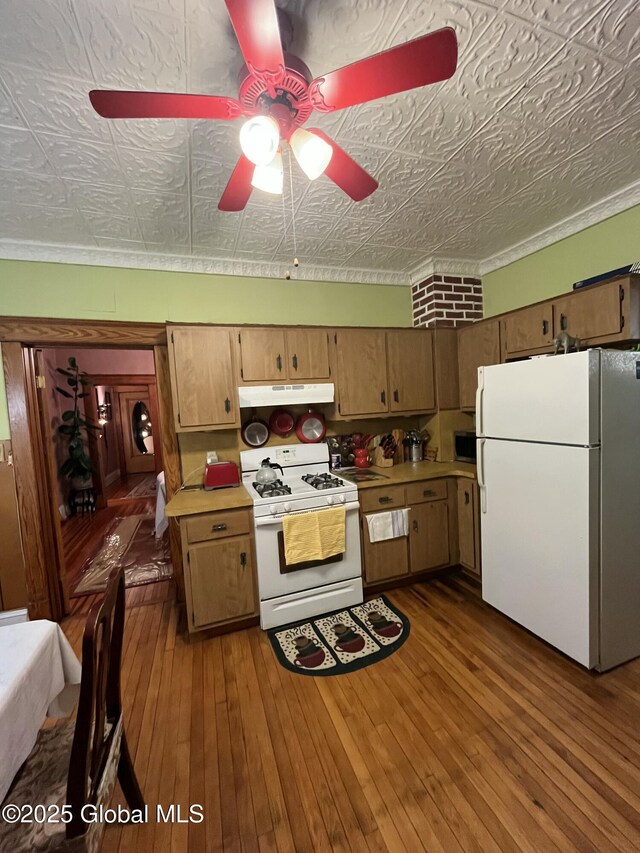 kitchen with under cabinet range hood, an ornate ceiling, white appliances, light countertops, and dark wood-style flooring