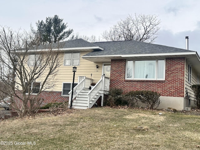 split level home featuring brick siding, roof with shingles, and a front lawn