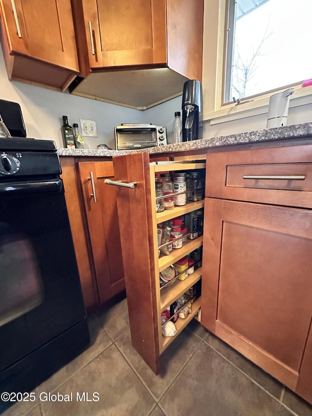 kitchen with dark tile patterned flooring, a toaster, light stone counters, brown cabinets, and range