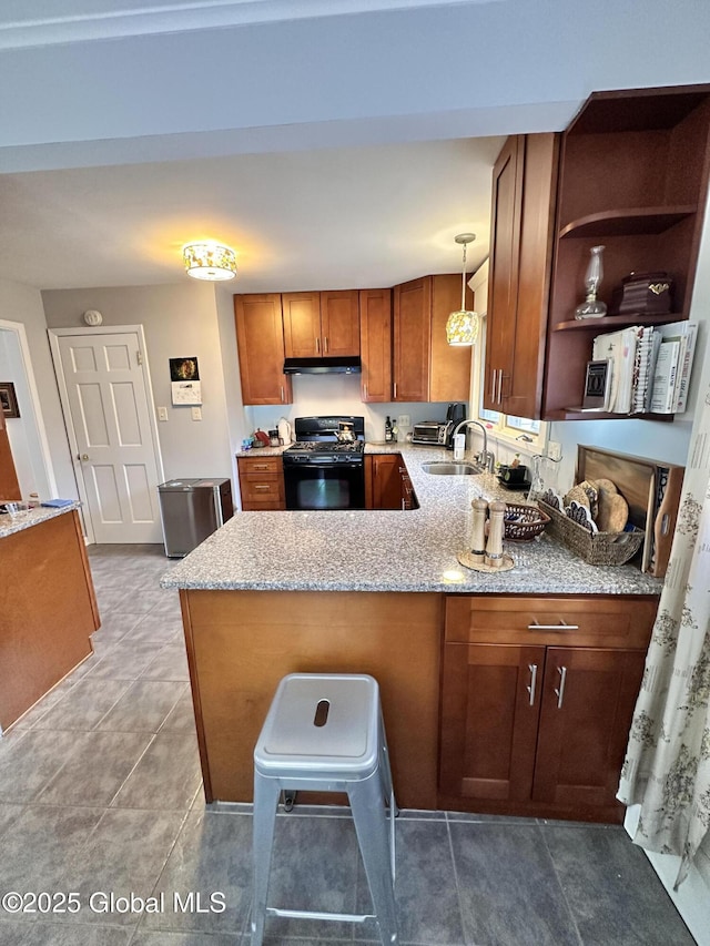 kitchen with brown cabinets, under cabinet range hood, gas stove, a peninsula, and light stone countertops