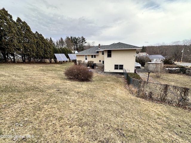 rear view of house with solar panels, fence, and a shingled roof