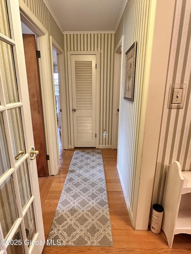hall with light wood-type flooring, wallpapered walls, and crown molding