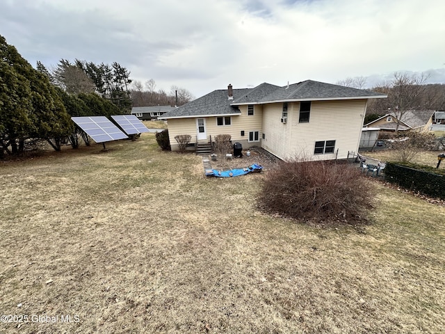 back of house with roof with shingles, solar panels, a chimney, and fence
