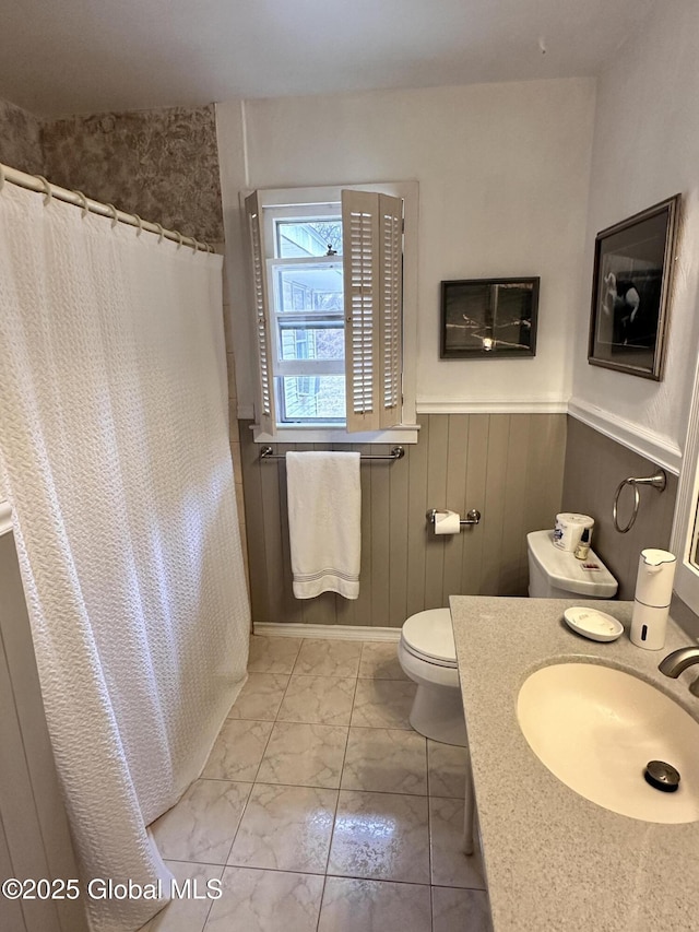 full bath with toilet, marble finish floor, a shower with shower curtain, wainscoting, and vanity