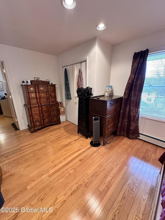 bedroom with recessed lighting, light wood-type flooring, baseboard heating, and a closet
