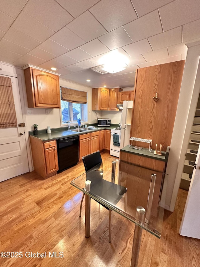 kitchen featuring dark countertops, light wood-type flooring, brown cabinets, white appliances, and a sink