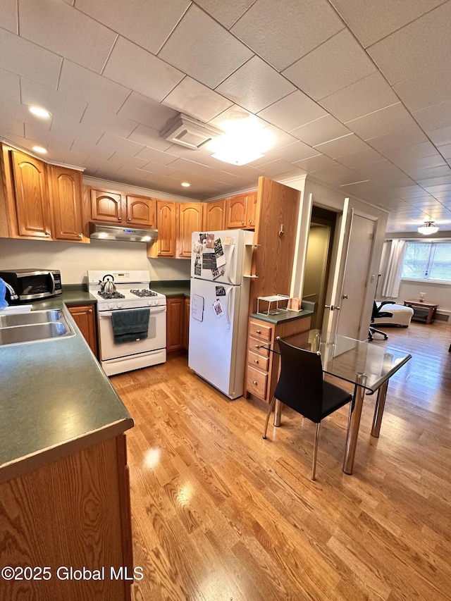 kitchen with dark countertops, under cabinet range hood, light wood-style floors, white appliances, and a sink