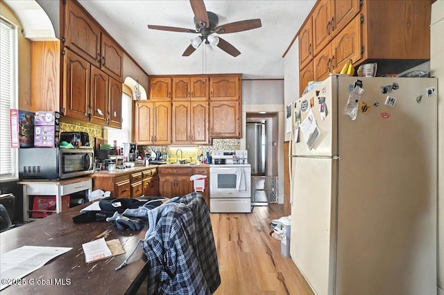 kitchen featuring a sink, tasteful backsplash, white appliances, light wood-style floors, and ceiling fan