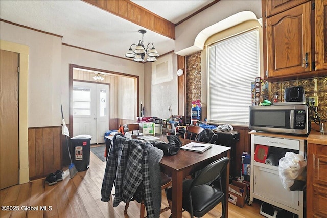 dining space with wooden walls, crown molding, a wainscoted wall, light wood-style flooring, and a notable chandelier