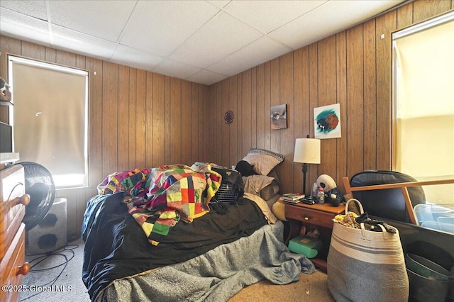 carpeted bedroom featuring a drop ceiling and wood walls