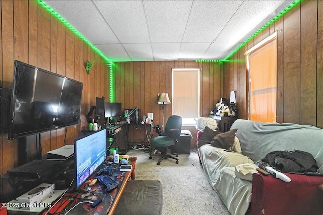 office with a paneled ceiling, light carpet, and wood walls