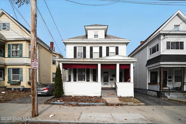 american foursquare style home featuring aphalt driveway, covered porch, and roof with shingles