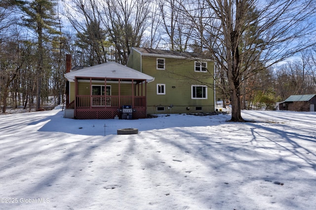 snow covered house with an outbuilding, covered porch, and a chimney