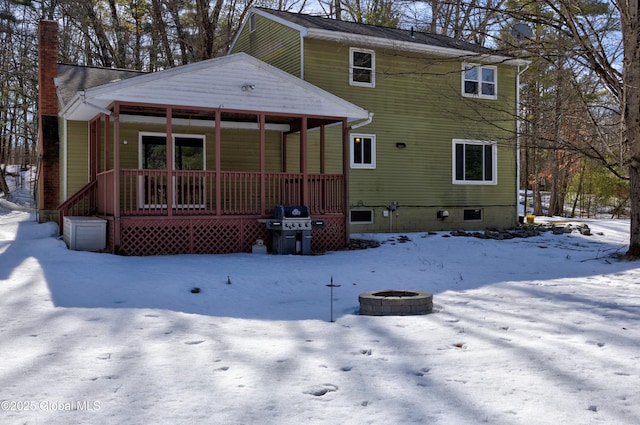 snow covered property featuring a porch, a chimney, and an outdoor fire pit