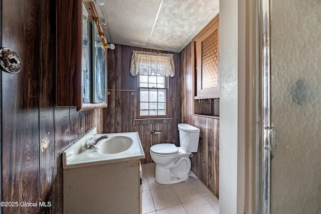 bathroom featuring vanity, tile patterned flooring, wood walls, a textured ceiling, and toilet