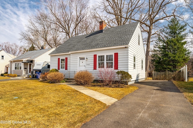 view of front of house featuring a front yard, fence, driveway, roof with shingles, and a chimney