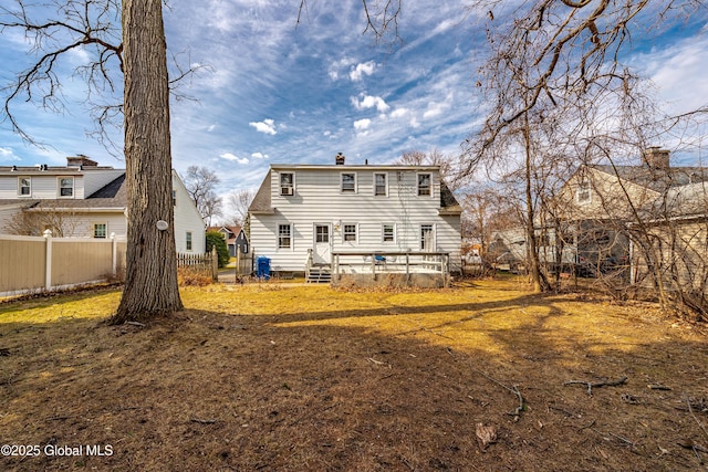 rear view of property featuring a wooden deck, a chimney, a yard, and fence