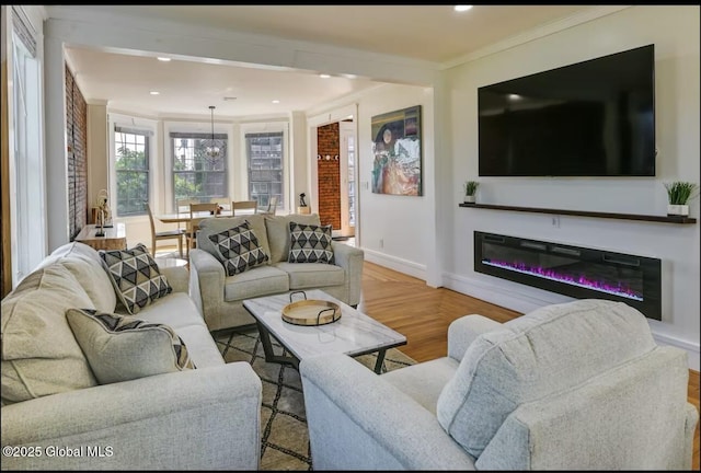 living area featuring wood finished floors, baseboards, recessed lighting, ornamental molding, and a glass covered fireplace