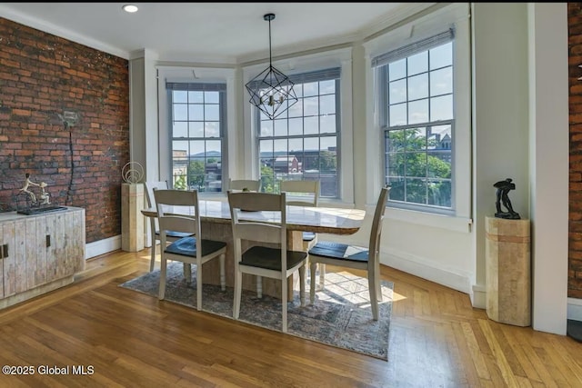 dining space featuring brick wall, baseboards, ornamental molding, light wood-style floors, and a notable chandelier