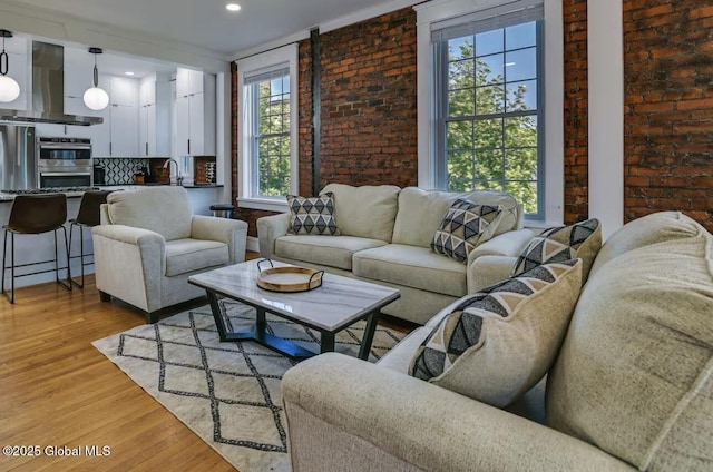 living area featuring light wood-style floors, brick wall, and ornamental molding