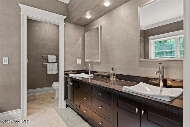 full bathroom featuring double vanity, toilet, baseboards, and a sink