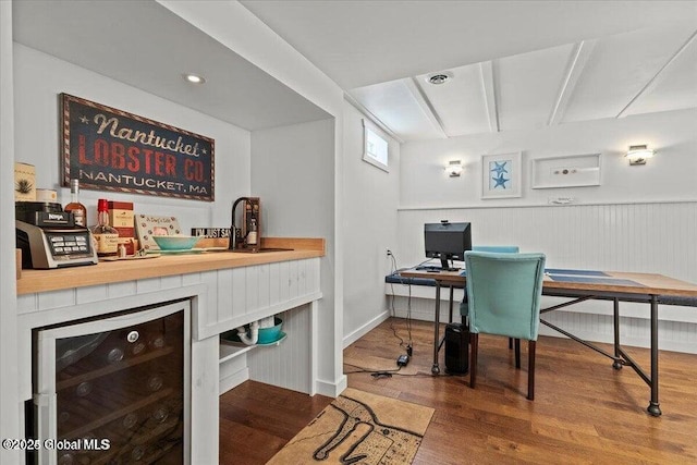 office space featuring a wainscoted wall, wine cooler, a bar, and wood finished floors