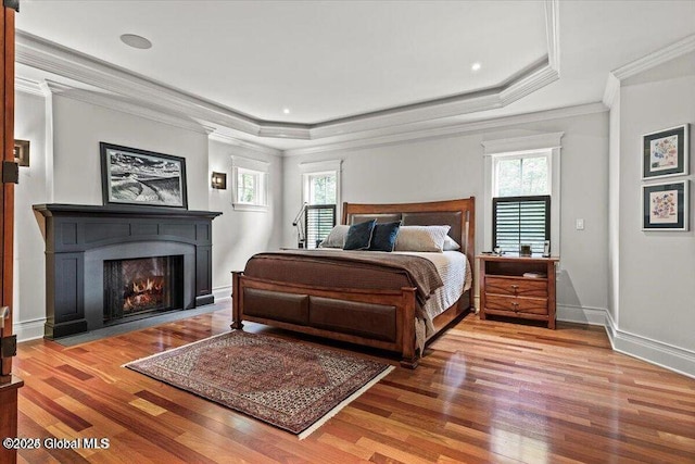 bedroom with crown molding, a raised ceiling, baseboards, and wood finished floors