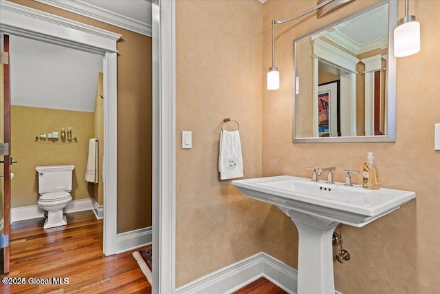 bathroom featuring toilet, wood finished floors, baseboards, and ornamental molding