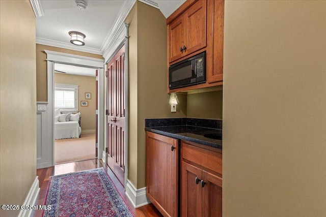 kitchen with brown cabinetry, dark wood-type flooring, ornamental molding, and black microwave