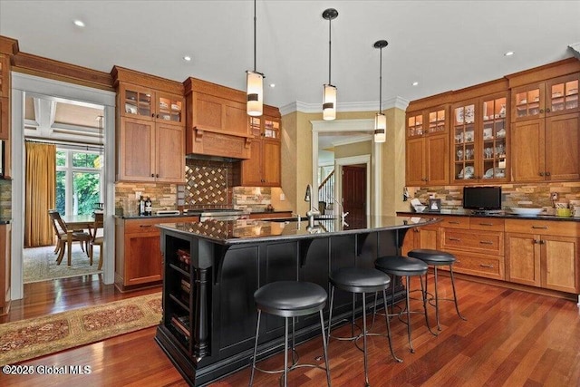 kitchen with a center island with sink, dark countertops, dark wood-style floors, and brown cabinetry