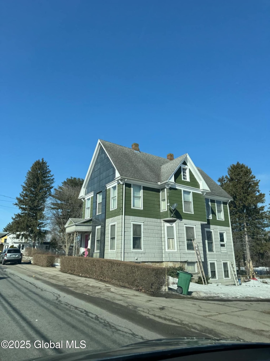 victorian house featuring roof with shingles and a chimney