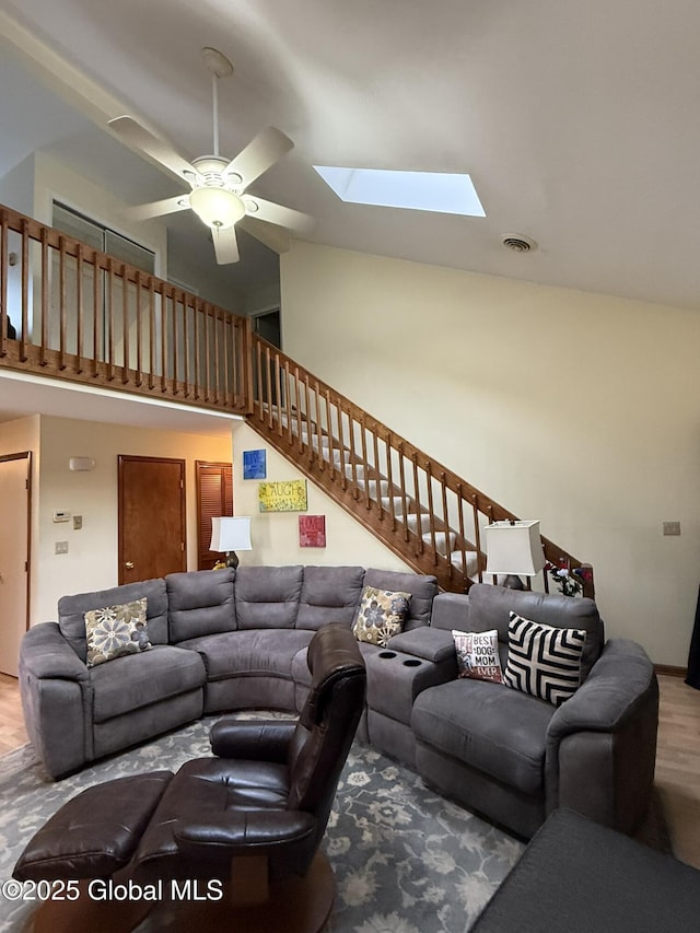 living room with visible vents, ceiling fan, stairs, a skylight, and high vaulted ceiling