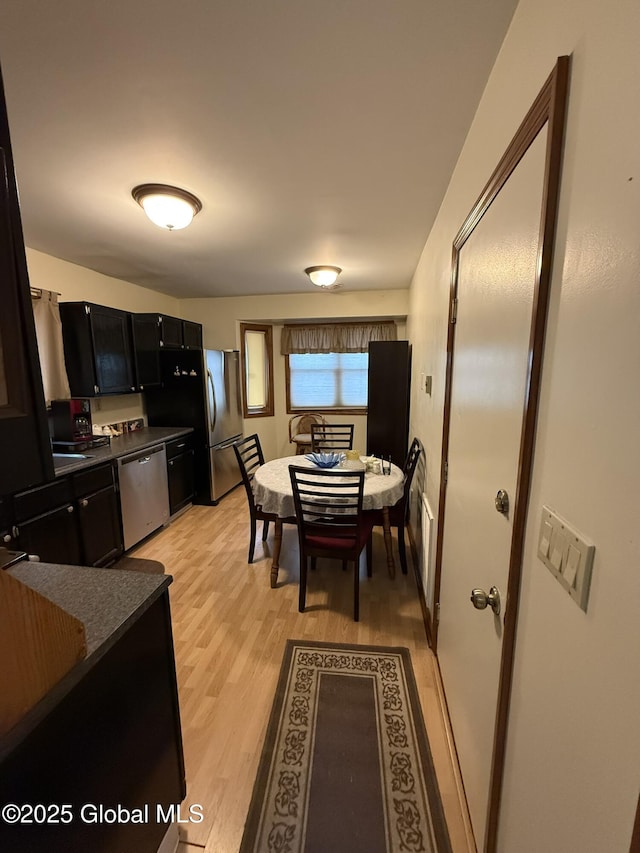 kitchen featuring stainless steel appliances, dark countertops, dark cabinetry, and light wood finished floors