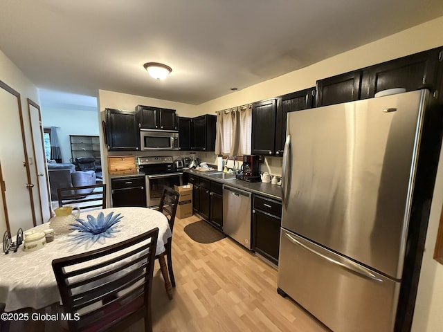 kitchen with dark cabinetry, light wood-style flooring, a sink, stainless steel appliances, and dark countertops