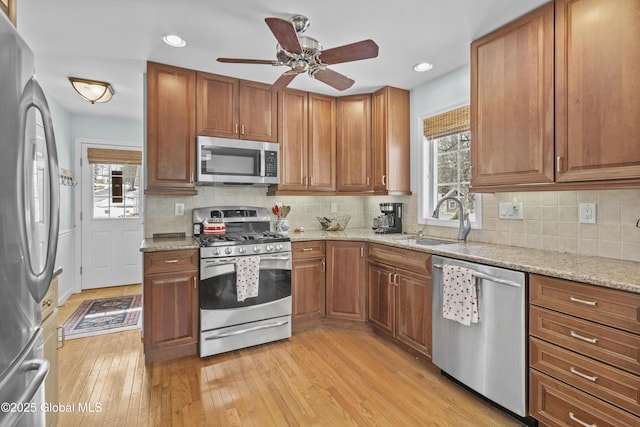 kitchen with light wood finished floors, brown cabinets, stainless steel appliances, a ceiling fan, and a sink