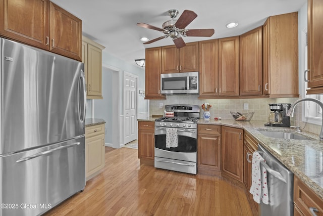 kitchen featuring a ceiling fan, a sink, appliances with stainless steel finishes, light wood finished floors, and decorative backsplash