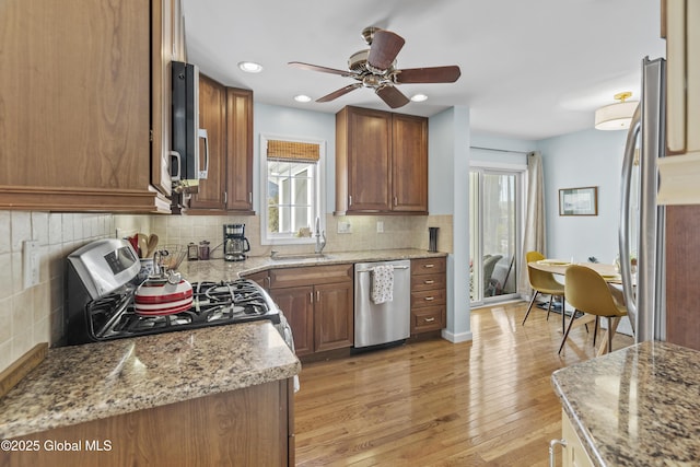 kitchen with a sink, appliances with stainless steel finishes, light wood finished floors, decorative backsplash, and ceiling fan