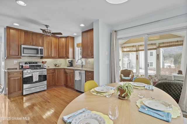 kitchen with backsplash, ceiling fan, light wood-style flooring, stainless steel appliances, and a sink