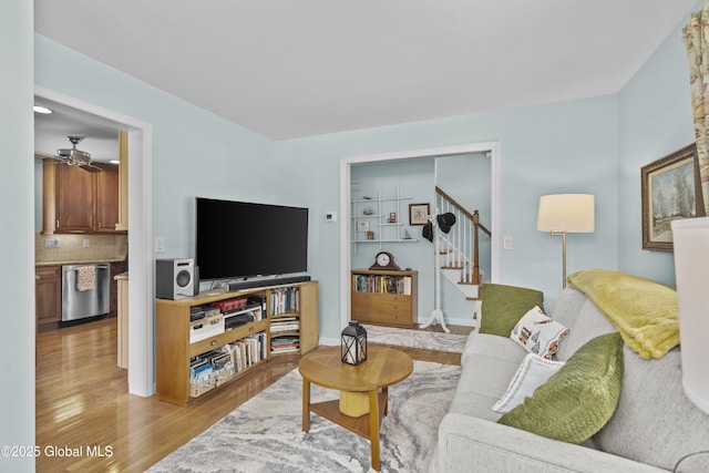 living room featuring ceiling fan, baseboards, light wood-style flooring, and stairs