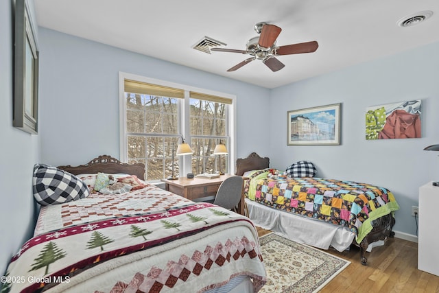 bedroom with ceiling fan, visible vents, baseboards, and wood finished floors