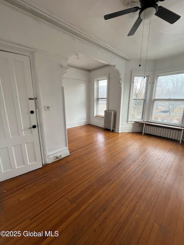 unfurnished living room featuring ornamental molding, radiator, baseboards, and hardwood / wood-style floors