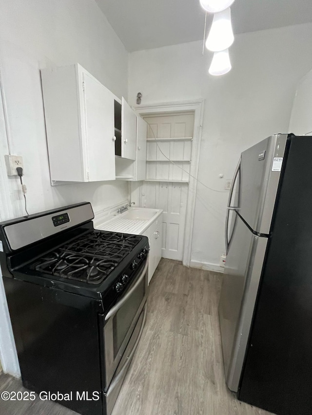 kitchen with light wood finished floors, a sink, stainless steel appliances, light countertops, and white cabinetry