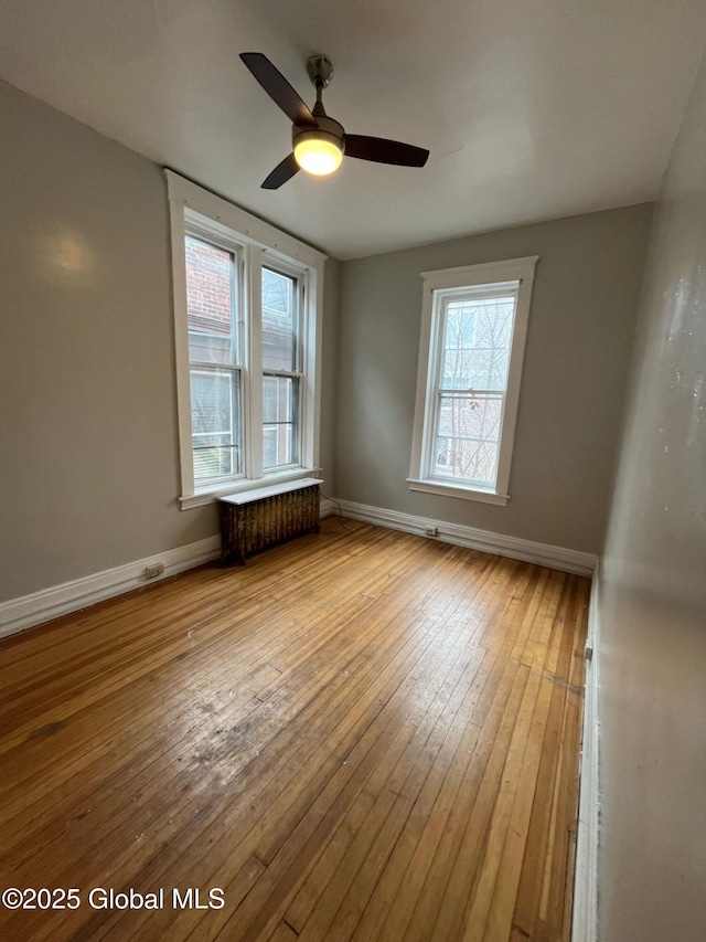 unfurnished room with baseboards, ceiling fan, radiator heating unit, and hardwood / wood-style flooring