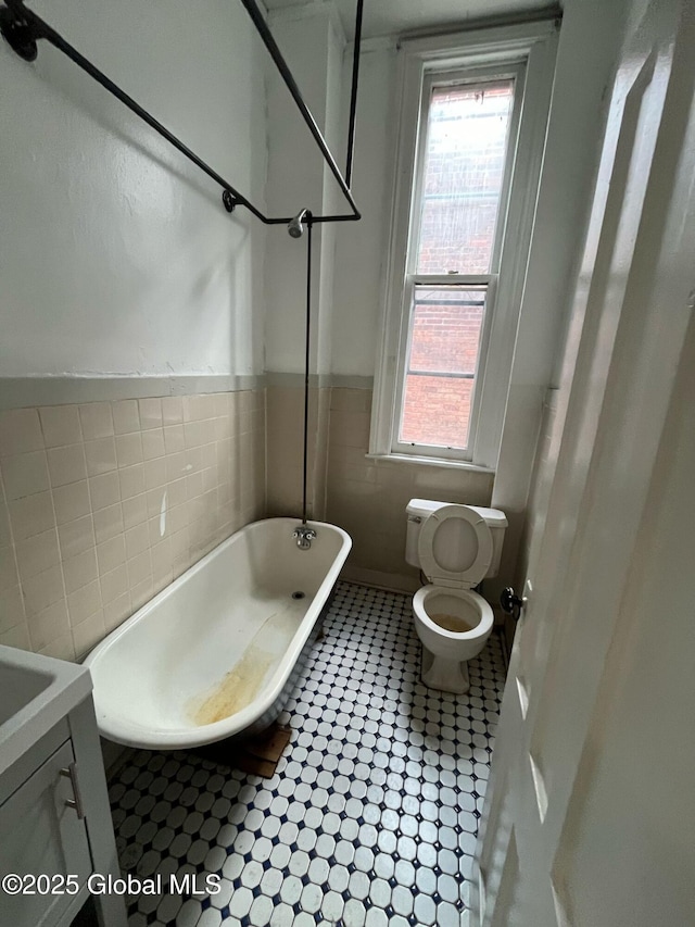 bathroom with tile walls, toilet, a tub to relax in, and plenty of natural light