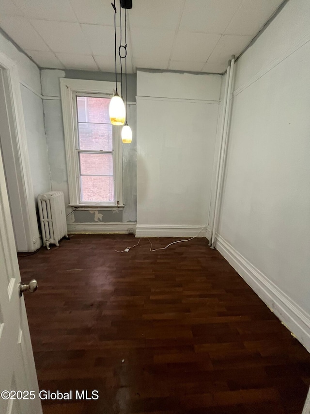 unfurnished dining area featuring radiator heating unit, dark wood-style floors, baseboards, and a paneled ceiling